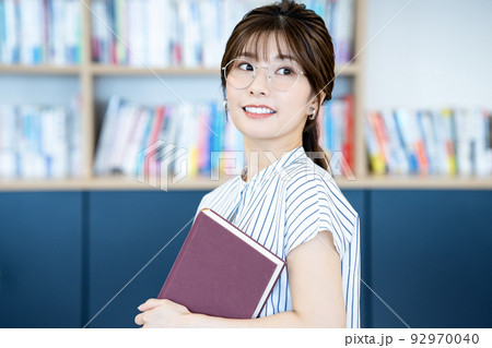 本を持つ眼鏡の若い女性 92970040