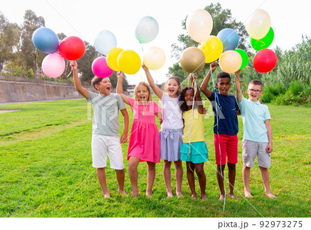 Barefoot kids playing with balloons on grass 92973275