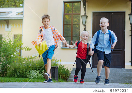 Happy caucasian children running from school with backpacks holding hands Begining of academic year. Boys and girl laughing plaing fool 92979054