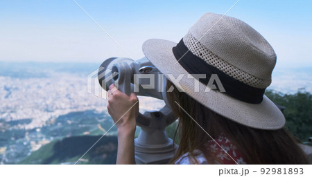 Unrecognizable woman traveler looking through viewing binoculars at summer city. Copy space. Woman in straw hat observes of blur panorama, with binoculars at observation deck. Mountain Dajti Albania Unrecognizable woman traveler looking through viewing binoculars at summer city. Copy space. Woman in straw hat observes of blur panorama, with binoculars at observation deck. Mountain Dajti Albania 92981893