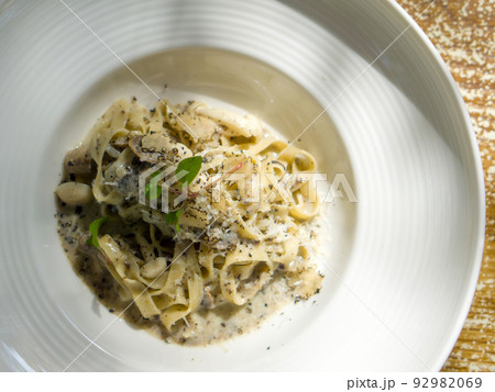 Tagliatelle Pasta with butter creamy white truffle sauce. Pasta with wild termite mushroom topped with truffle slice and watercress. Closeup italian food served on deep round plate. Top view Tagliatelle Pasta with butter creamy white truffle sauce. Pasta with wild termite mushroom topped with truffle slice and watercress. Closeup italian food served on deep round plate. Top view 92982069