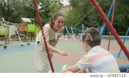 4K. Mom rides her son on a swing in the park in the summer 4K. Mom rides her son on a swing in the park in the summer 92982528