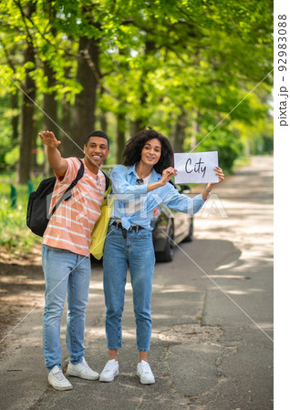 Dark-skinned couple hitchhiking on the road in the countryside Dark-skinned couple hitchhiking on the road in the countryside 92983088