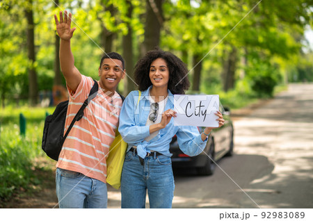 Dark-skinned couple hitchhiking on the road in the countryside Dark-skinned couple hitchhiking on the road in the countryside 92983089
