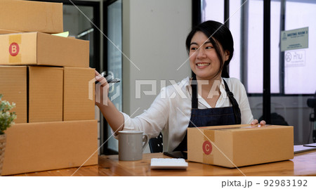 Smiling entrepreneur checking order on delivery box on work desk at home 92983192
