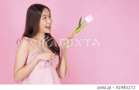 Satisfied excited asian woman holding tulips pointing up wonder to copy space smiling with toothy  92983272