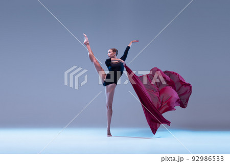 Portrait of young flexible ballerina dancing with deep red fabric isolated over blue grey studio background. Graceful Portrait of young flexible ballerina dancing with deep red fabric isolated over blue grey studio background. Graceful 92986533