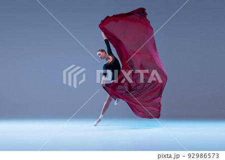 Portrait of young tender ballerina dancing with deep red fabric isolated over blue grey studio background. Lightness, grace Portrait of young tender ballerina dancing with deep red fabric isolated over blue grey studio background. Lightness, grace 92986573
