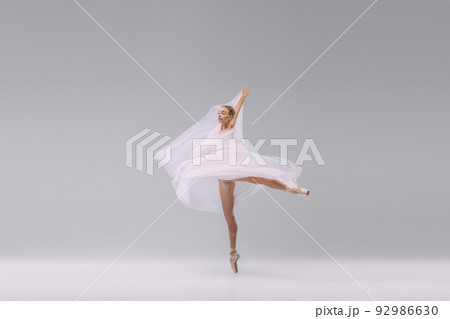 Portrait of young flexible ballerina dancing with transparent fabric isolated over grey studio background. Tenderness, grace 92986630