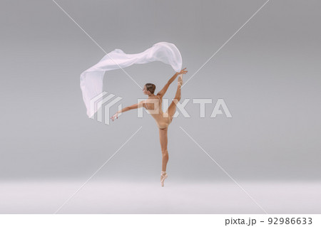 Portrait of young tender ballerina dancing in beige cloth with transparent fabric isolated over grey studio background. Looks weightless 92986633