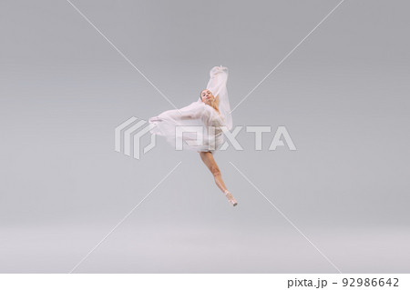 Portrait of young ballerina dancing, jumping with transparent fabric isolated over grey studio background. Leap 92986642