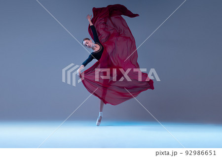 Portrait of young flexible ballerina dancing with fabric isolated over blue grey studio background. Tender deep red flower Portrait of young flexible ballerina dancing with fabric isolated over blue grey studio background. Tender deep red flower 92986651