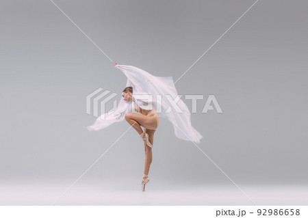 Portrait of young ballerina dancing with transparent fabric isolated over grey studio background. Tender movements Portrait of young ballerina dancing with transparent fabric isolated over grey studio background. Tender movements 92986658