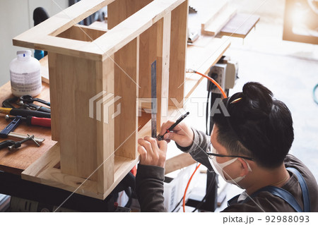 A carpenter measures the planks to assemble the parts, and build a wooden table for the customer. 92988093