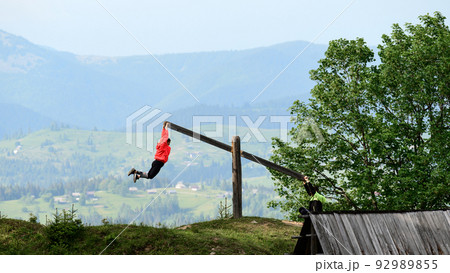 A boy and a girl are riding on a manual swing in the mountains. 92989855