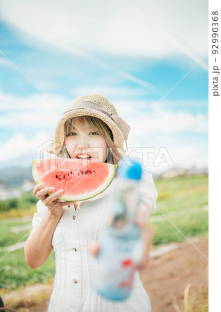 青空のもとスイカとラムネを持って夏を満喫する女性 92990368