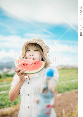 青空のもとスイカとラムネを持って夏を満喫する女性 92990371