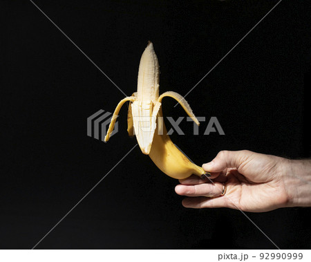 Hand holds peeled banana on dark background 92990999