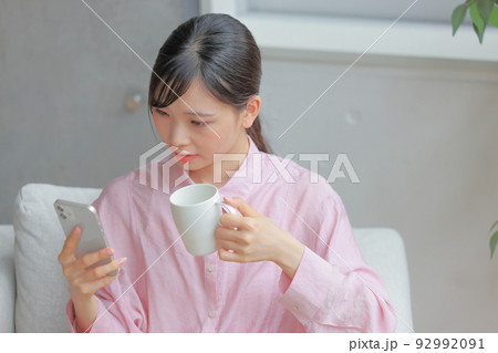 コーヒーカップを持ちスマホをけげんな表情で見る女性1 92992091