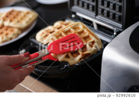 Pastry chef takes hot waffles from waffle iron in kitchen Pastry chef takes hot waffles from waffle iron in kitchen 92992610