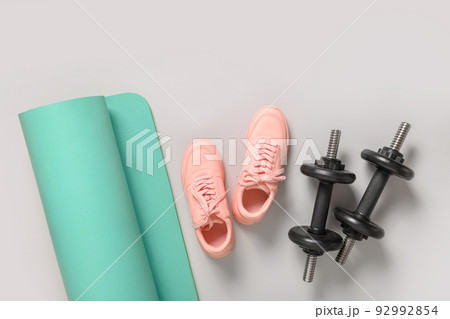 Sport and fitness equipment, female pink shoes, yoga mat on grey background. Sport and fitness equipment, female pink shoes, yoga mat on grey background. 92992854