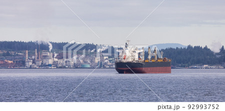 Industrial Processing Plant and Container Ship passing by on a cloudy day. Industrial Processing Plant and Container Ship passing by on a cloudy day. 92993752