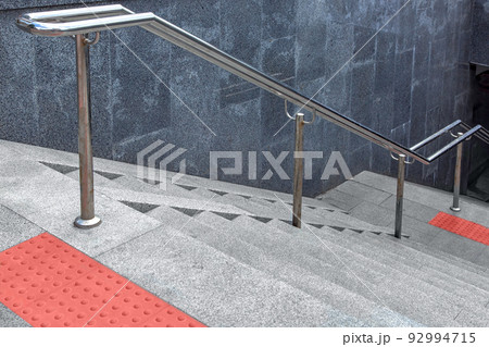 stainless steel iron handrail descent to underground crossing with granite staircase and wall and stone steps, entrance to subway with tactile tiles and ramp for disabled, close-up view, nobody. stainless steel iron handrail descent to underground crossing with granite staircase and wall and stone steps, entrance to subway with tactile tiles and ramp for disabled, close-up view, nobody. 92994715