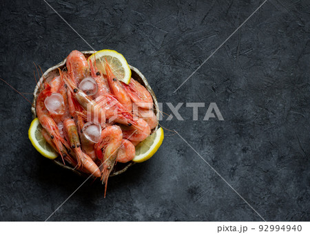Raw shrimps with lemon and ice on a dark background. Raw shrimps with lemon and ice on a dark background. 92994940