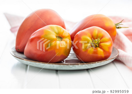 Bull heart tomatoes on plate on white table. 92995059