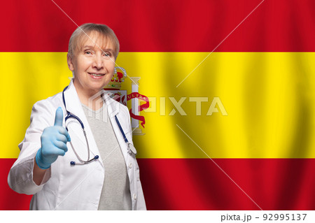 Spanish smiling mature doctor woman holding stethoscope on flag of Spain background 92995137