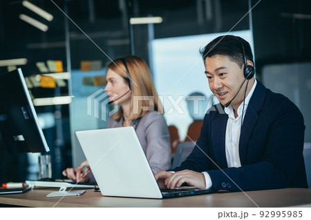 Happy call center employee communicates with customers, advises on video call, remotely, asian business man Happy call center employee communicates with customers, advises on video call, remotely, asian business man 92995985