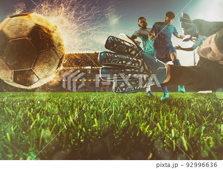 Close up of a soccer scene at night match with a goalkeeper trying to catch a fiery ball Close up of a soccer scene at night match with a goalkeeper trying to catch a fiery ball 92996636
