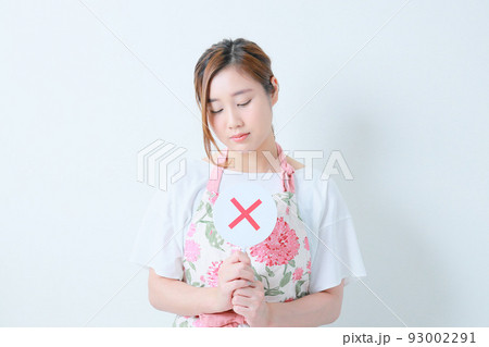 胸の前で✖️札を両手で持つ悲しげな女性 93002291