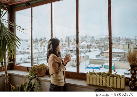 woman enjoy coffee standing next to a window with beautiful view of snowy landscape woman enjoy coffee standing next to a window with beautiful view of snowy landscape 93002570