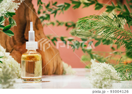 Amber glass dropper bottle of serum or oil in nature. Leaves and flowers on pink 93004126