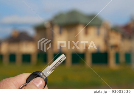 Close up of woman hand with keys on the background of a blurred house. New own house concept Close up of woman hand with keys on the background of a blurred house. New own house concept 93005339