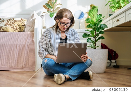 Mature woman sitting on the floor at home looking at laptop Mature woman sitting on the floor at home looking at laptop 93006150