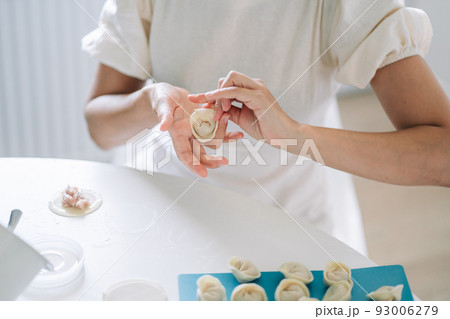 Woman making dumplings. Front view of woman's hands making meat dumpling. Cook hands lay out minced meat on dumplings Woman making dumplings. Front view of woman's hands making meat dumpling. Cook hands lay out minced meat on dumplings 93006279