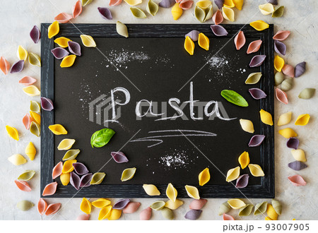 Multi-coloured Italian pasta conchiglie or seashells with basil leaves on chalk board. Word Pasta wrote with chalk 93007905