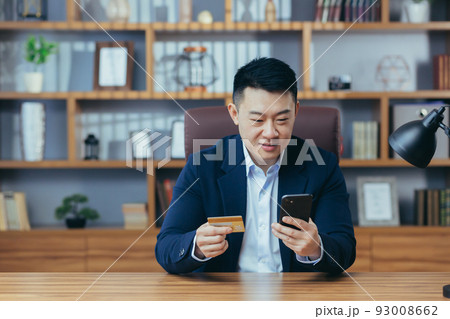 Happy Asian shopping online sitting in the office, man using phone app and bank card, businessman enjoying online shopping Happy Asian shopping online sitting in the office, man using phone app and bank card, businessman enjoying online shopping 93008662