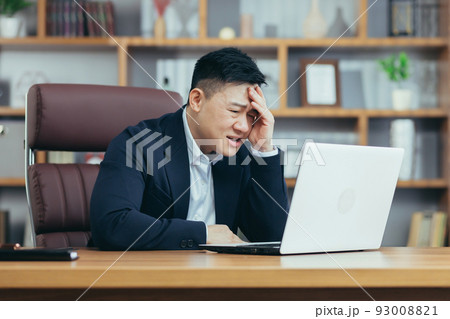 Frustrated and angry asian businessman working on laptop in office, boss shouting at laptop screen Frustrated and angry asian businessman working on laptop in office, boss shouting at laptop screen 93008821