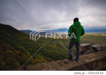 a man traveling on foot, standing in a bright jacket on top mountain 93010419