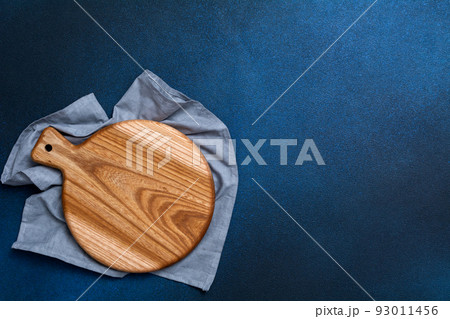Wooden cutting board on a blue napkin on a dark blue background. Kitchenware top view. Empty space for your ready meals. 93011456