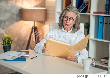 Gray-haired woman sitting at the table and working with project documentation Gray-haired woman sitting at the table and working with project documentation 93014013