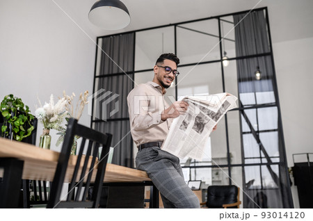 Smiling man with newspaper leaning on table Smiling man with newspaper leaning on table 93014120