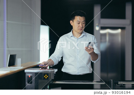 Successful Asian businessman worker enters office, uses key card to open turnstile, man looks at phone screen reads news 93016194