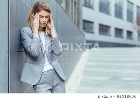 Business woman near office building outside, has severe headache, tired and depressed holding hands behind head 93018656