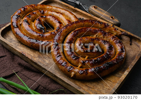 Homemade Spiral grilled sausage with spices and herbs, on wooden tray, on black dark stone table background Homemade Spiral grilled sausage with spices and herbs, on wooden tray, on black dark stone table background 93020170