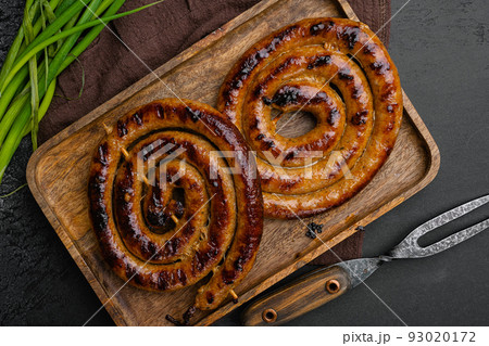 Grilled sausages spiral, on wooden tray, on black dark stone table background, top view flat lay Grilled sausages spiral, on wooden tray, on black dark stone table background, top view flat lay 93020172