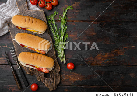 Hot dog grilled sausage in a bun with sauces, on old dark  wooden table background, top view flat lay, with copy space for text 93020342